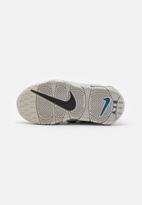 Suela de zapatilla Nike en blanco y gris, con un diseño texturizado que presenta patrones de agarre en forma de círculo y el logo swoosh en negro. Acentuada con azul.