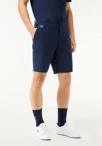 Pantalones cortos de color navy hechos de una tela ligera, con bolsillos frontales, cierre de cremallera y un pequeño logo verde en la cintura.
