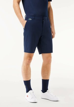Pantaloni corti navy realizzati in tessuto leggero, con tasche frontali, chiusura con zip e un piccolo logo verde sulla vita.