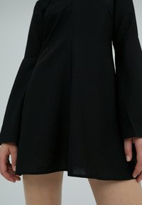 Robe noire à manches longues en forme de cloche, fabriquée dans un tissu léger, avec une silhouette évasée et une texture subtile.