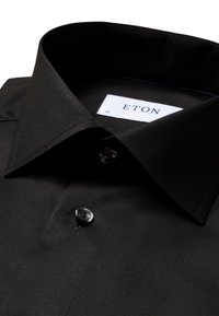 Svart skjorte med spiss krage, med en enkelt knappåpning og Eton-merke. Glatt stoff, minimalistisk design og uten mønster.