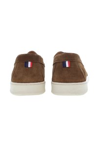 Bruna mockaskor med en vit gummisula. Baksidan har ett litet franskt flagga-emblem. Minimalistisk design med mjuk textur.