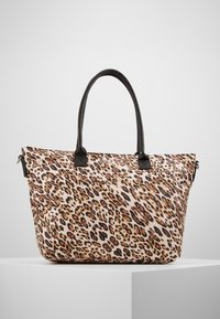 Grand sac fourre-tout avec un motif léopard et des poignées noires exposé sur un piédestal blanc contre un fond uni.