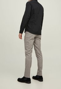 Camicia nera a maniche lunghe abbinata a pantaloni a quadri grigi chiari. I pantaloni presentano sottili righe rosse e blu; gli stivali neri alla caviglia completano il look.
