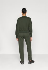 Hanorac verde cu mâneci raglan, cu mansete și tiv țesute. Asortat cu pantaloni jogger verzi. Materialul pare moale și texturat.