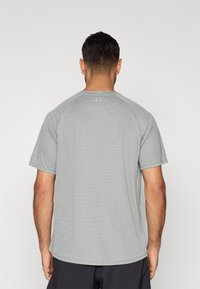 Αθλητική γκρι ανοιχτόχρωμη μπλούζα με ριμπ υφή, κοντά μανίκια και στρογγυλή λαιμόκοψη. Διακριτικό λογότυπο στο πίσω μέρος κοντά στη λαιμόκοψη.