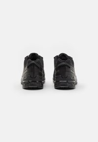 Black athletic shoes featuring a mesh upper, padded collar, and textured sole with distinct tread patterns for grip and stability.