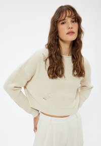 Crème gebreide trui met een cropped ontwerp. Bevat een gestructureerd patroon en verouderde details op de mouwen en het lijf.