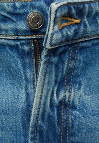 Denim tkanina u srednje plavoj boji s zatvaračem i metalnim dugmetom za zatvaranje. Sadrži vidljive šavove u kontrastnoj smeškastoj boji za dodatne detalje.