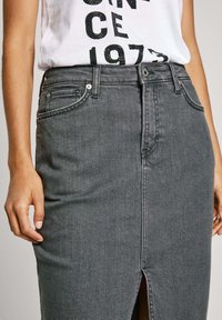 Grijze denim kokerrok met een split aan de voorkant, hoge taille, riemlussen en stikseldetails. Gecombineerd met een wit grafisch T-shirt.