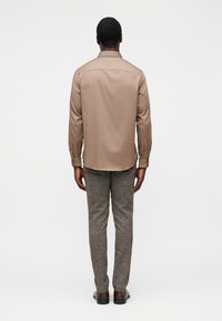 Μπεζ ανοιχτό καφέ μακρυμάνικο πουκάμισο με ίσια γραμμή, συνδυασμένο με υφασμάτινο γκρι παντελόνι με υφή και καφέ παπούτσια, φωτογραφημένο από πίσω.