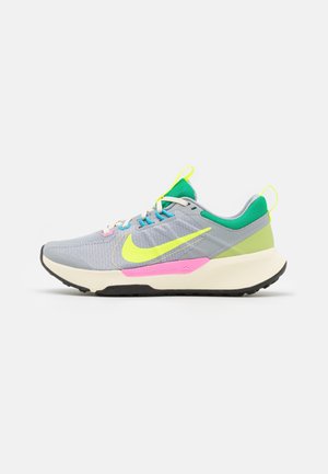 Hellgrauer Sportschuh mit neongelbem Nike-Swoosh, pinkfarbenem Zwischensohlen-Akzent, grünem Innenfutter und schwarzer Sohle, von der Seite gesehen.