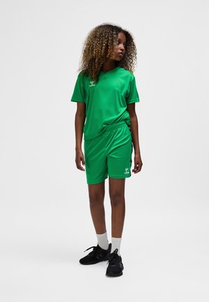 Grünes Sportoutfit bestehend aus einem kurzärmligen Oberteil und Shorts, aus glattem Stoff gefertigt, mit einem Logo auf der Brust und am linken Bein.