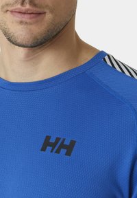 Modrý sportovní tričko s texturovanou tkaninou, černé logo na přední straně a pruhovaný akcent na ramenou. Zaoblený výstřih a krátké rukávy.