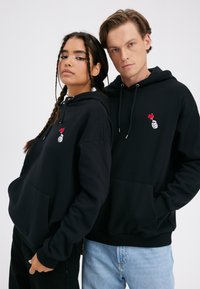 Black hoodies made of soft fabric with a front pocket, featuring a red heart graphic, worn by two models with different jeans styles.