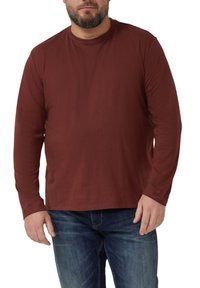 Długi rękaw t-shirt z ciemnobordowego materiału, z okrągłym dekoltem i gładką fakturą. W połączeniu z niebieskimi dżinsami.