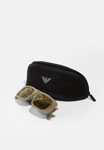 Lunettes de soleil beiges avec des verres imprimés léopard, accompagnées d'une housse zippée noire portant un logo. Matériau en plastique, forme rectangulaire.