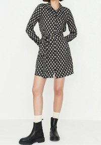 Dlouhé černé šaty s bílým vzorem srdcí, límečkem, páskem v oblasti pasu a předním rozparkem. Kombinováno s černými kotníkovými botami a krémovými ponožkami.