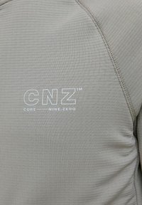 Šviesiai pilka sportinė maikutė su faktūrine medžiaga, kurią puošia balta "CNZ" logotipas ir "CORE NINE.ZERO" tekstas priekyje. Matomi siūlių detalės.