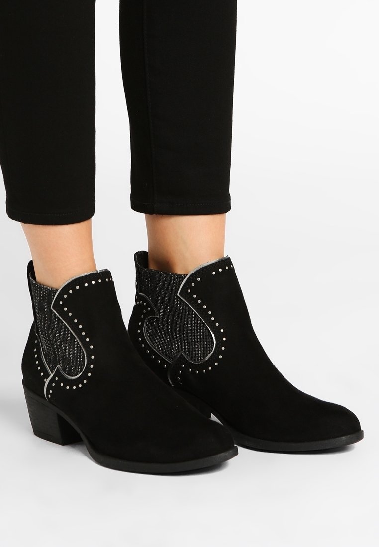 Bottes basses en daim noir avec un panneau métallique texturé, des coutures décoratives et des clous en accent. Talon bas carré et bout pointu.