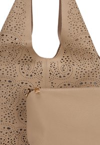 Beige leren tote bag met laser-geperforeerde openingen in spiraalpatronen, één ritsvak op de voorkant en een soepele textuur.