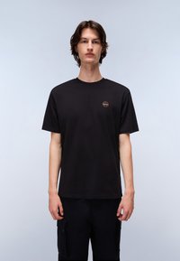 Zwarte katoenen T-shirt met een ronde hals en korte mouwen, voorzien van een klein rond logo op de bovenste linkerzijde. Eenvoudig ontwerp.