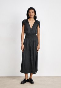 Robe maxi noire avec un décolleté en V profond, des manches bouffantes, une taille élastique et une fermeture à boutons sur le devant. Tissu lisse et design longueur cheville.