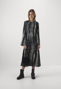 Rochie cu mânecă lungă tie-dye în nuanțe de negru și gri, cu un croi lejer; asociată cu botine negre până la glezne și o geantă cu franjuri texturate.