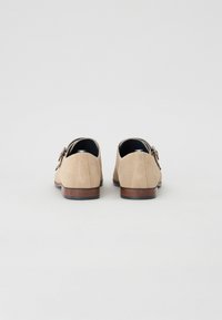 Beige Wildlederschuhe mit glatter Oberfläche, runder Zehenform und Holzabsatz. Sie verfügen über eine silberfarbene Schnallenverzierung an der Seite.