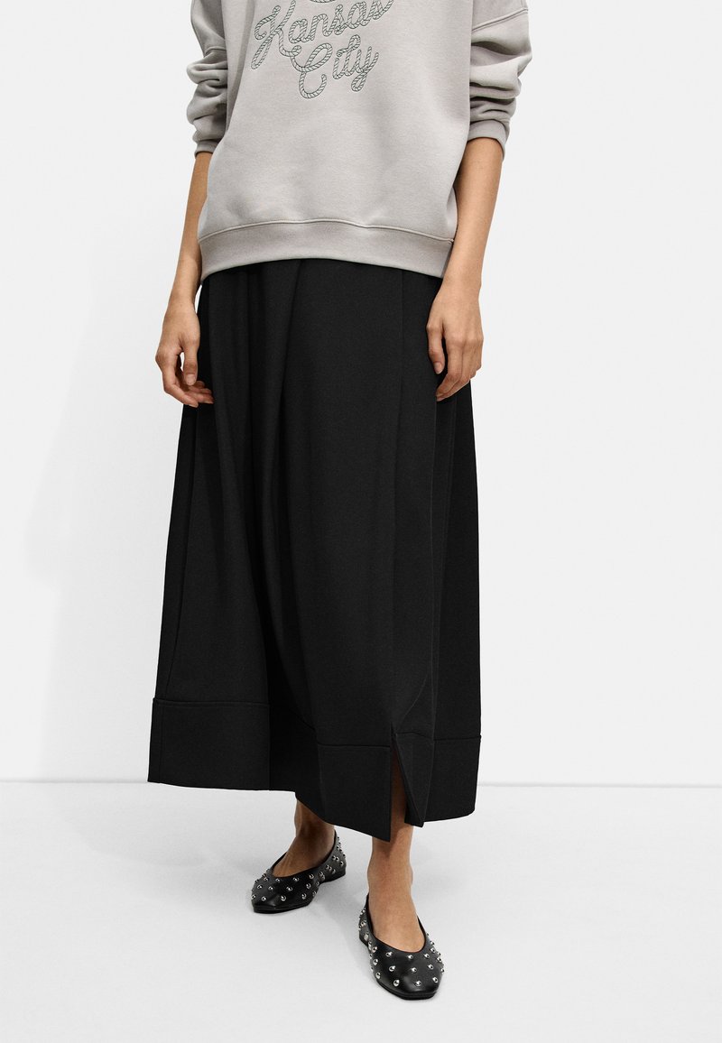 Czarna spódnica do kostek z bocznymi rozcięciami, wykonana z miękkiego materiału. Połączona z szarym dresowym swetrem z napisem "Kansas City" metaliczną nicią.