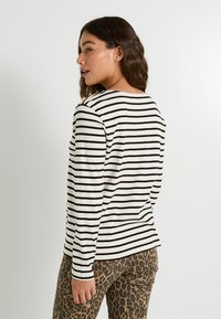 Blusa de manga larga en color crema con rayas negras, con escote redondeado y detalles de botones en el hombro, combinada con pantalones de estampado de leopardo.
