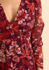 Blumenkleid mit tiefem V-Ausschnitt, Dreiviertelärmeln und einer Mischung aus roten und lila Farben in einem strukturierten Stoff.