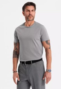 T-shirt grigio a maniche corte realizzato in cotone morbido, abbinato a pantaloni grigi, con una cintura nera e un orologio al polso.