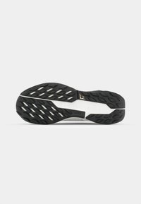 Semelle d'une chaussure de sport noire avec une surface en caoutchouc texturé, des accents blancs contrastants et un motif de semelle unique pour une meilleure adhérence.