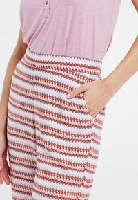 Patronenbroek met een geometrisch ontwerp in roze, rood en zwart, inclusief een zak. Gemaakt van lichtgewicht stof en voorzien van een elastische tailleband.