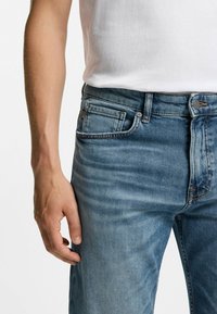 Pantalones vaqueros de mezclilla azul claro con un diseño clásico de cinco bolsillos, un patrón de desvanecimiento sutil, con un botón de cobre y detalles de costura.