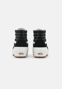 Czarne zamszowe wysokie trampki z białymi paskami, akcentami w kratkę na podeszwie i wyraźnymi detalami w szwie. Logo Vans na pięcie.