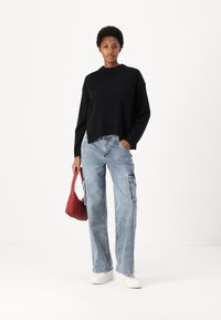 Črna pletena jopica z visokim ovratnikom, v kombinaciji z svetlo modrimi cargo hlačami. Dodatki vključujejo majhno rdečo torbico in bele superge.