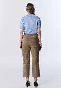 Un pull court à manches courtes bleu clair avec un col côtelé, associé à un pantalon en daim marron au fit décontracté et avec des détails de couture visibles.