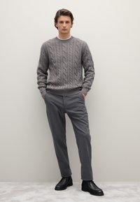 Maglione grigio a maglia con colletto a costine, abbinato a pantaloni grigi su misura e stivaletti in pelle nera. Design semplice e moderno.