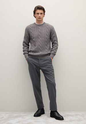 Grauer Kabelstrick-Pullover mit gerippten Bündchen, kombiniert mit maßgeschneiderten grauen Hosen und schwarzen Lederstiefeletten. Schlichte und moderne Gestaltung.