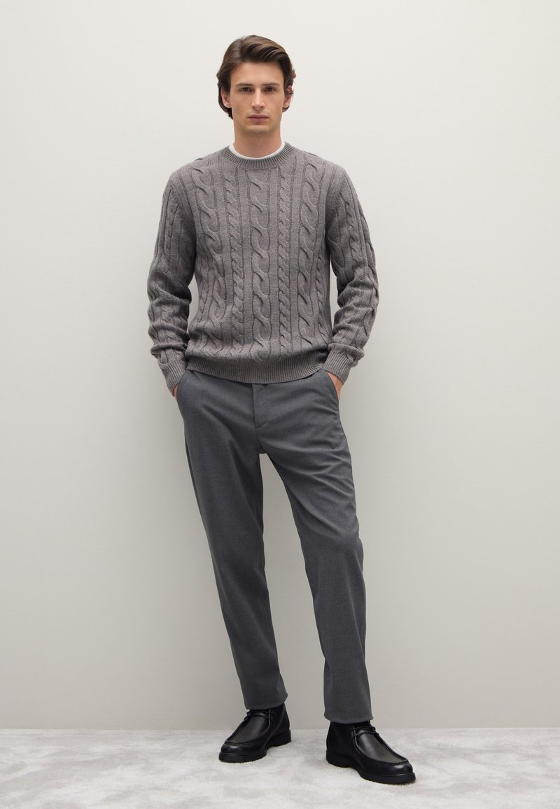 Maglione grigio a maglia con colletto a costine, abbinato a pantaloni grigi su misura e stivaletti in pelle nera. Design semplice e moderno.