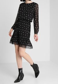 Černé květinové šaty s dlouhými průhlednými rukávy, volánkovým lemem a krajkovým lemem. Vytvořeno s lesklými černými kotníkovými botami.