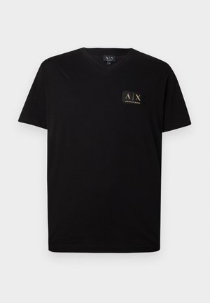 Svart V-hals T-skjorte laget av myk bomull. Har en liten, gullfarget logo-patch på venstre bryst. Korte ermer og avslappet passform.