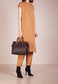 Lichtbruin jurkje met korte mouwen, gecombineerd met aangesloten broeken, zwarte laarzen met een slouch- stijl, en een zwarte handtas met gouden accenten.