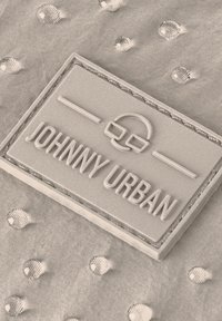Tessuto grigio chiaro strutturato caratterizzato da gocce in rilievo e un'etichetta in gomma rettangolare impressa con "JOHNNY URBAN" e accenti minimalisti.