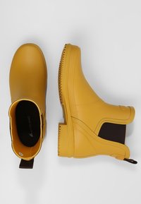 Botas de tobillo de goma amarillas con lados elásticos, textura lisa y forma curva. Suela acanalada para mayor tracción. Diseño clásico de botas de lluvia.