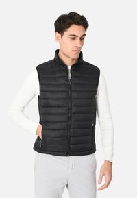 Gilet imbottito nero con colletto alto, chiusura a zip frontale e tasche laterali. Presenta una texture trapuntata e un design aderente per il massimo del calore.