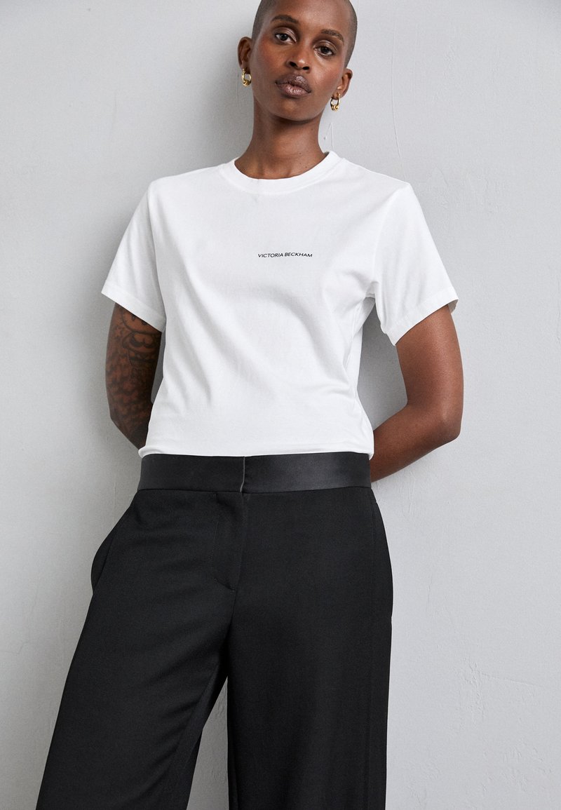 Camiseta de algodón blanca con mangas cortas y escote redondo, con "Victoria Beckham" impreso en pequeño en color negro en la parte frontal.