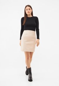 Černý přiléhavý top s dlouhým rukávem, kombinovaný s lehkou béžovou koženou áčkovou sukní a černými masivními botami na podpatku. Jednoduchý design, hladká textura.